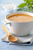 Close-up of Bowl of Pumpkin Soup on Tea Towel with Wooden Spoon on Blue Background,Studio Shot