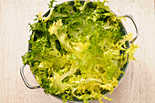 Draufsicht auf Salat im Sieb für Salat auf beigem Hintergrund, Studioaufnahme