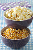 Schalen mit Maiskörnern und Popcorn auf blauem Gingham-Hintergrund, Studioaufnahme