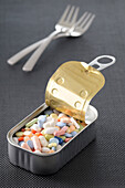 Variety of Pills in Opened Tin with Forks in Background,Studio Shot
