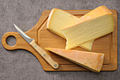 Wedges of Raclette Cheese with Knife on Wooden Cutting Board