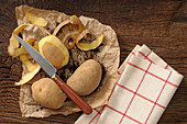 Draufsicht auf Kartoffeln, die mit Messer und Geschirrtuch geschält werden, Studioaufnahme