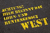 Close-up of German text on paved road (Attention,Here begins the area of wage and pension West),Berlin,Germany