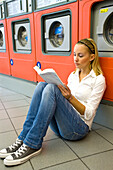Frau liest ein Buch in einem Waschsalon
