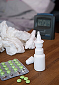 Medication and crumpled facial tissues and alarm clock on bedside table,studio shot