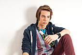 Teenage boy wearing headphones around neck and holding bottle of beer,studio shot on white background