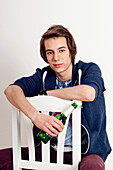 Portrait of teenage boy sitting on chair holding bottle of beer,smiling and looking at camera,studio shot on white background