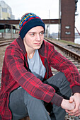 Close-up portrait of teenage boy sitting on railroad tracks near harbour,Germany