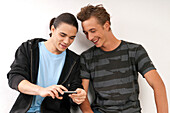 Zwei junge Männer, Freunde, die zusammen auf ihr Handy schauen, Studioaufnahme auf weißem Hintergrund