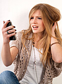 Junge, blonde, langhaarige Frau starrt ungläubig auf ihr Handy, Studioaufnahme auf weißem Hintergrund
