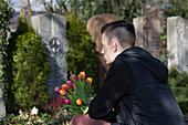 Teenager Crouching in front of Grave Stones in Cemetery