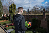 Teenager mit Tulpen vor Grabsteinen auf dem Friedhof stehend
