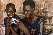 Lehrlinge benutzen ein Mobiltelefon in einer Werkstatt in Fatick, Senegal, Westafrika, Afrika
