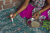 Adivasi-Frau klebt Perlen auf einen Sari in einem Dorf im Narmada-Distrikt, Gujarat, Indien, Asien