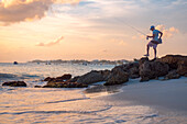 Ein einheimischer Fischer bei Sonnenuntergang mit ruhigem Wasser und orangefarbenem Himmel an der Südküste von Barbados, Westindien, Karibik, Mittelamerika