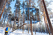 Blick auf einen Touristen, der den würfelförmigen Raum mit Spiegelwand in einem mit Eis und Schnee bedeckten borealen Wald bewundert, Baumhotel, Harads, Lappland, Schweden, Skandinavien, Europa