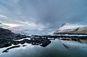 Snow covered mountains and rock pool reflections at low tide,Gjogv village,Eysturoy Island,Faroe Islands,Denmark,Europe