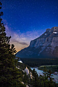 The Hoodoos formation near Banff,Alberta,on the Tunnel Mountain Drive,overlooking the Bow River and Mount Rundle,with the stars and Milky Way in the sky. Illumination is by starlight,twilight sky colours,and lights from Banff in the distance. The sky is bright and blue with summer twilight,and from the waxing Moon low in the sky behind Mount Rundle.