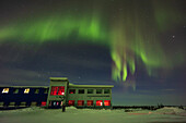 Aurorale Vorhänge im Norden über dem Churchill Northern Studies Centre, mit einem einsamen Fotografen beim Aufbau. Dies war am 25. Februar 2023 vom Parkplatz aus.