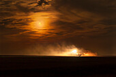 Der abnehmende gibbous Mond in den Wolken über einem Mähdrescher bei der Arbeit in einem Weizenfeld, am 2. September 2023.