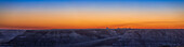 Dies ist ein Panorama des farbenfrohen Abenddämmerungshimmels über den Badlands des Red Deer River, Alberta, aufgenommen vom Aussichtspunkt Horsethief Canyon nördlich von Drumheller auf dem Dinosaur Trail. Die sehr dünne Mondsichel ist auf dem Foto, aber schwer zu erkennen. Es ist eine blasse Mondsichel, die sehr tief im orangefarbenen Schein rechts von den Getreidesilos ganz links zu sehen ist.