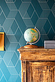 Old wooden cupboard in front of geometrically patterned wallpaper in blue with globe