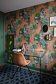 Study with glass desk and velvet chair in front of a wall with floral wallpaper