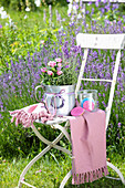 Weißer Gartenstuhl mit Lavendel (Lavandula) und rosa Rosen in Metallkanne