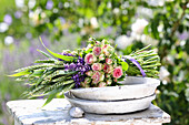 Bouquet of roses (Rosa), lavender (Lavandula) and ears of corn on wooden stool in the garden