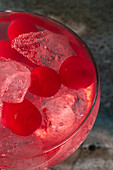 Red cocktail with ice cubes and cherries