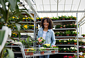 Lächelnde junge Frau in Gärtnerei mit Blumentöpfen