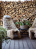 Cosy seating area with sheepskin armchairs in front of a stack of firewood