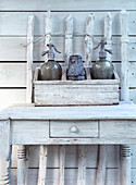 Vintage siphon bottles and metal jug on a wooden console in front of a white-painted wooden wall