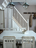 Dining area with white wooden table and chairs, industrial hanging lamps and rustic wall decoration