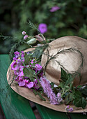 Straw hat with pink vetches (Lathyrus) and purple spurflower (Liatris) on a green bench