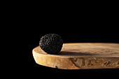 A whole black winter truffle on a wooden board