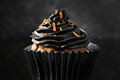 Close-up of a cupcake with black cocoa icing sprinkled with orange zest