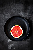 Rose grapefruit half on a black plate
