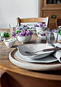 Wooden table setting with white plates and purple flower arrangements