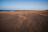 Ein Paar geht am Strand spazieren, während ein starker Wind Sand auf Lanzarote, Kanarische Inseln, Spanien, weht