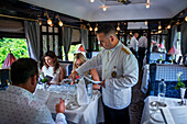 A waiter serves water and food in the art deco restaurant wagon of the train Belmond Venice Simplon Orient Express luxury train.