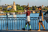 Touristen am Fluss Guadalquivir und der Torre del Oro, was übersetzt Turm aus Gold heißt - historisches Wahrzeichen aus dem XIII Jahrhundert in Sevilla, Andalusien, Spanien