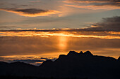 Eine Sonnensäule bei Sonnenaufgang über den Bergen, verursacht durch Licht, das von Eiskristallen in der Atmosphäre reflektiert wird. Quartzsite, Arizona