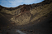 Volcan del Cuervo (Krähenvulkan) ein Krater, der auf einem Rundweg in einer kargen, felsigen Landschaft erkundet wird