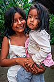 Ein Mädchen kümmert sich um ihre Schwester, während ihre Eltern arbeiten, einheimische Familie im Flussuferdorf Timicuro I. Iqutios, peruanischer Amazonas, Loreto, Peru