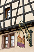 Frankreich, Haut Rhin, Route des Vins d'Alsace, Riquewihr mit der Bezeichnung Les Plus Beaux Villages de France (Eines der schönsten Dörfer Frankreichs), Fassade eines Fachwerkhauses und Ladenschild