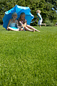 Mädchen mit blauem Schirm auf dem Rasen sitzend