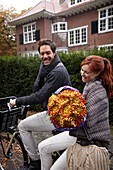 Couple riding bicycle holding flowers