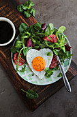 Heart-shaped fried egg with salami and salad