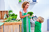 Woman preparing green vegetables and salad with her son in the kitchen